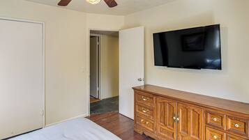 Un dormitorio con cama, cómoda de madera, televisor de pantalla plana en la pared y ventilador de techo.