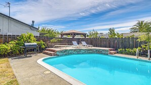 Un giardino con piscina, barbecue e un patio in legno.