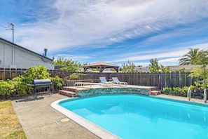 Un patio trasero con piscina, una parrilla y una terraza de madera.