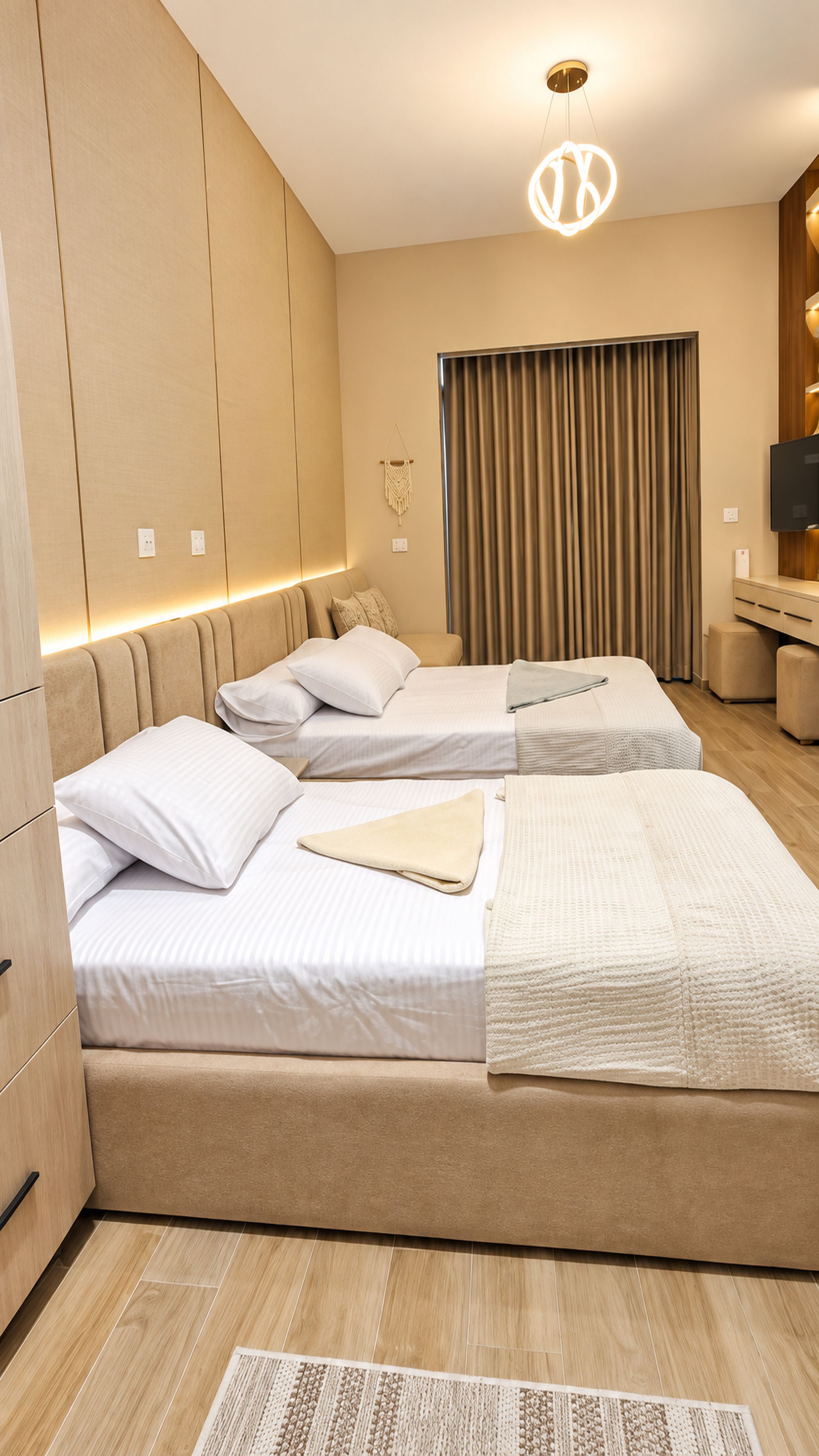 Ein Hotelzimmer mit zwei Betten, einem großen Fenster mit Vorhängen, einem Flachbildfernseher und Holzboden.