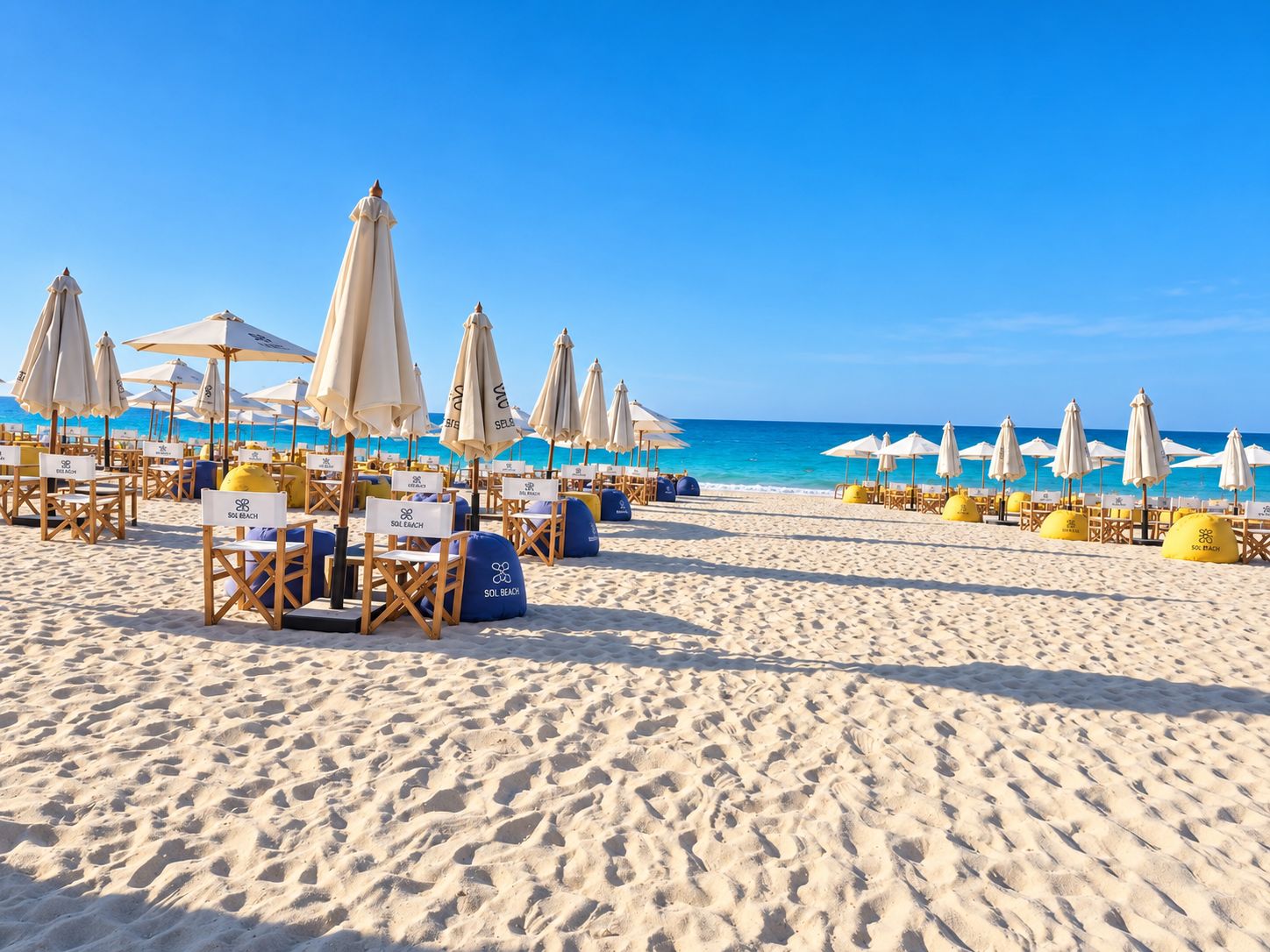 Ein Strand mit mehreren Reihen Sonnenliegen und Sonnenschirmen, einige mit dem Schriftzug 'SOL BEACH'.