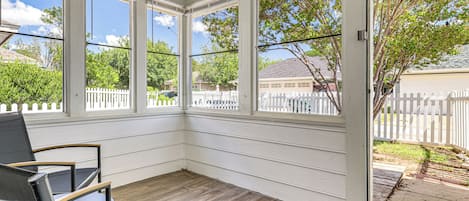 Eine überdachte Veranda mit Blick auf einen weißen Zaun und einen Baum.