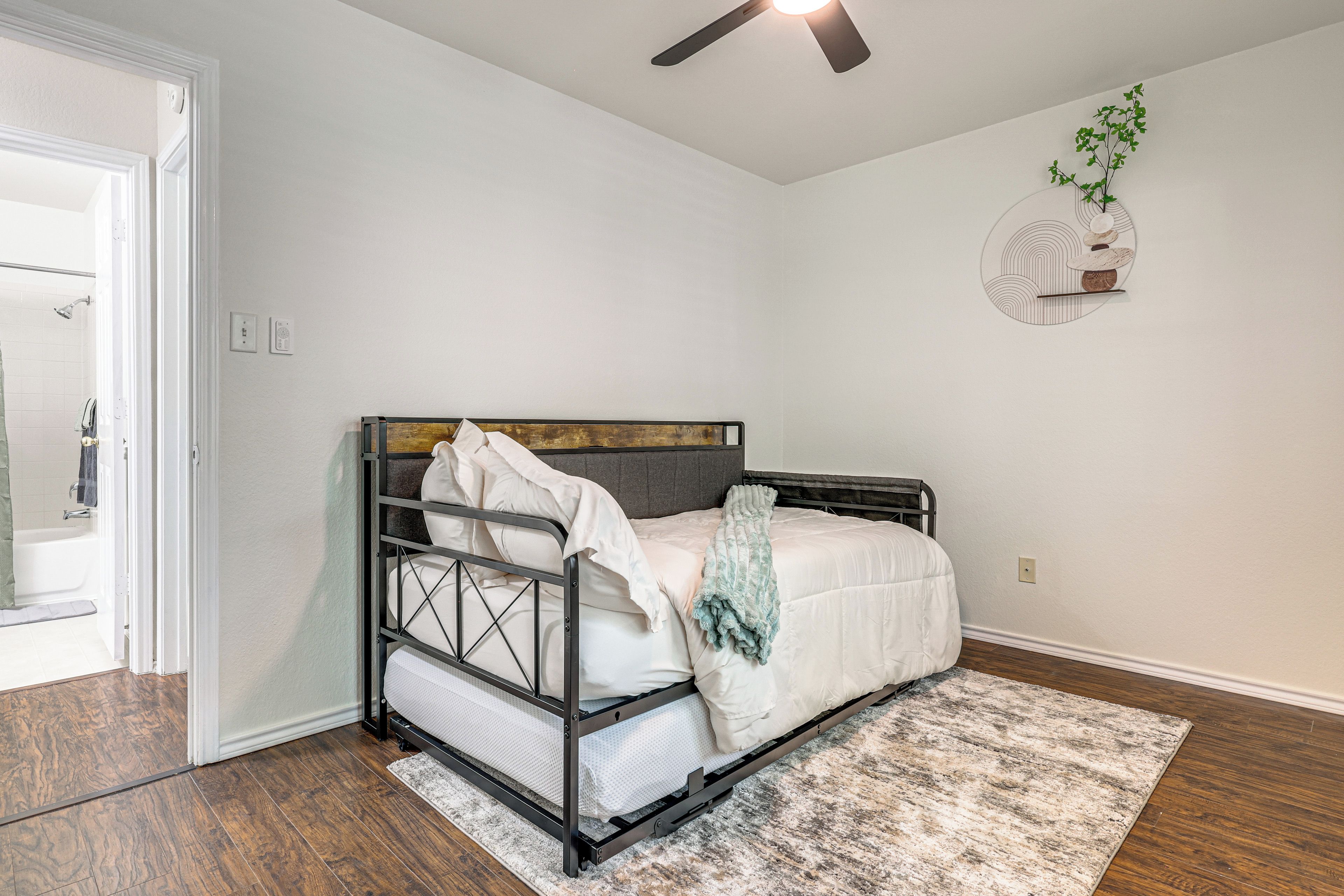 A bedroom with a bed, a ceiling fan, a wall-mounted plant, and a bathroom visible through an open door.