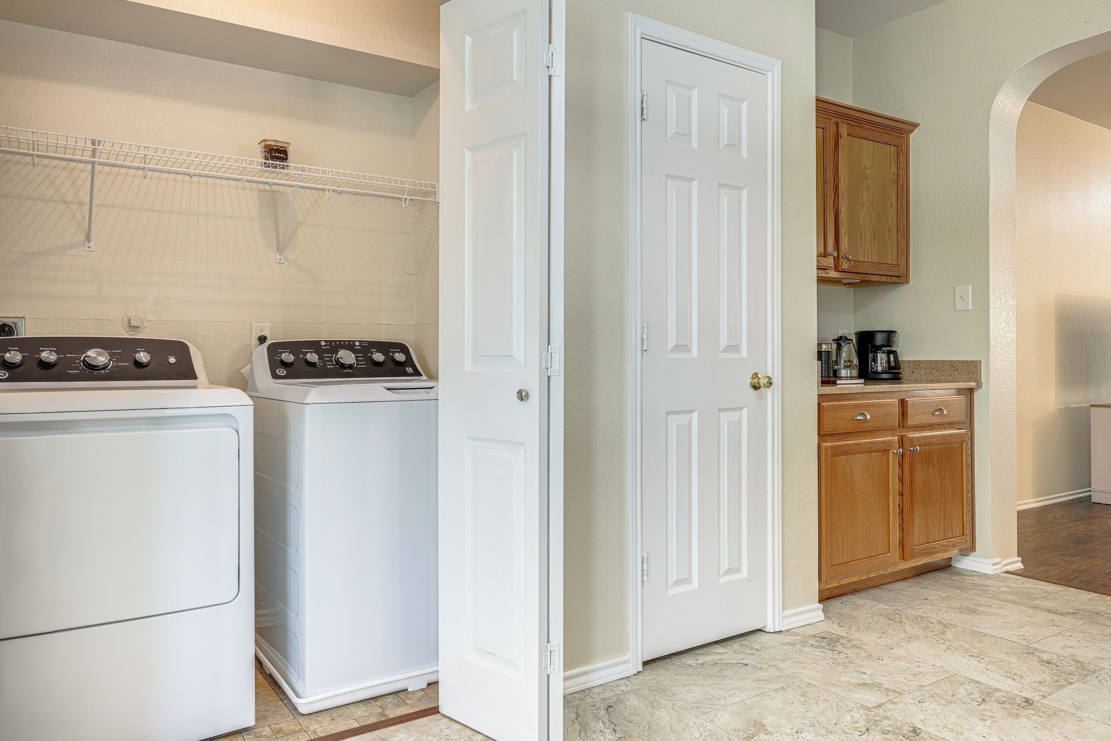 A laundry area with two front-loading washers and dryers, a white door, wooden cabinets, and a countertop with a coffee maker.