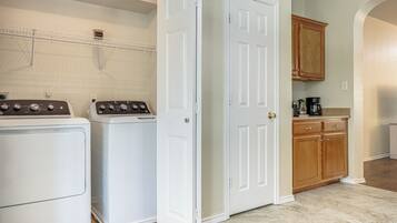 A laundry area with two front-loading washers and dryers, a white door, wooden cabinets, and a countertop with a coffee maker.