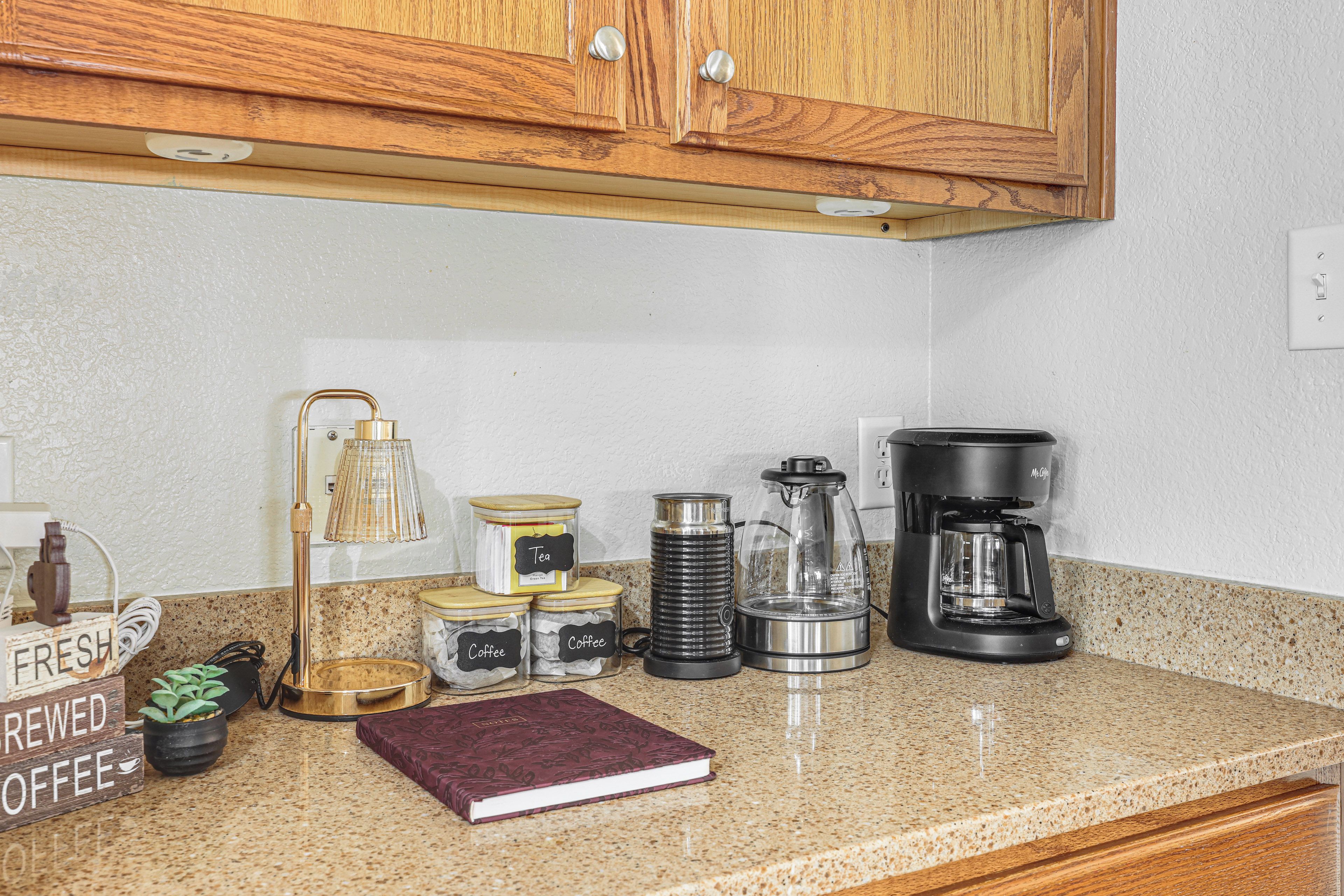 A kitchen counter with coffee-making equipment, including a coffee maker, a kettle, and jars labeled 'Coffee' and 'Tea'.