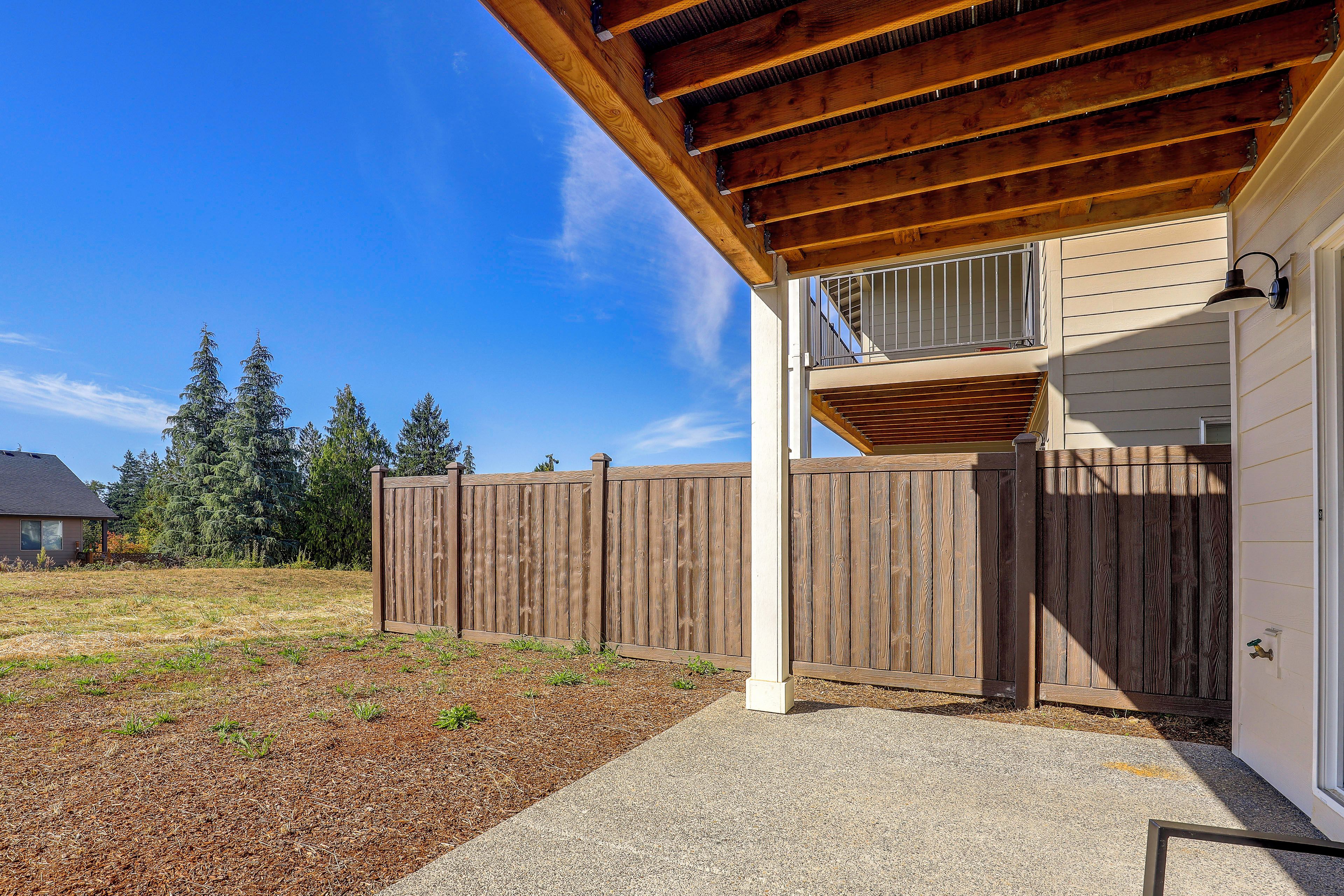 A wooden deck with a covered area, a wooden fence, and a house with a window.