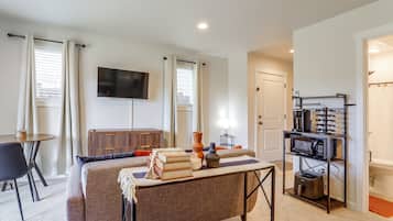 A modern living room with a flat-screen TV, a coffee machine, and a dining area with a table and chairs.
