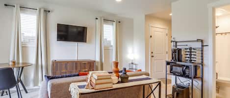 A modern living room with a flat-screen TV, a coffee machine, and a dining area with a table and chairs.