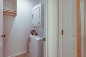 A laundry room with a front-loading washer and dryer, a towel rack, and a door leading to another room. - PNW Home Base! Gresham Studio w/ Patio (Gresham)