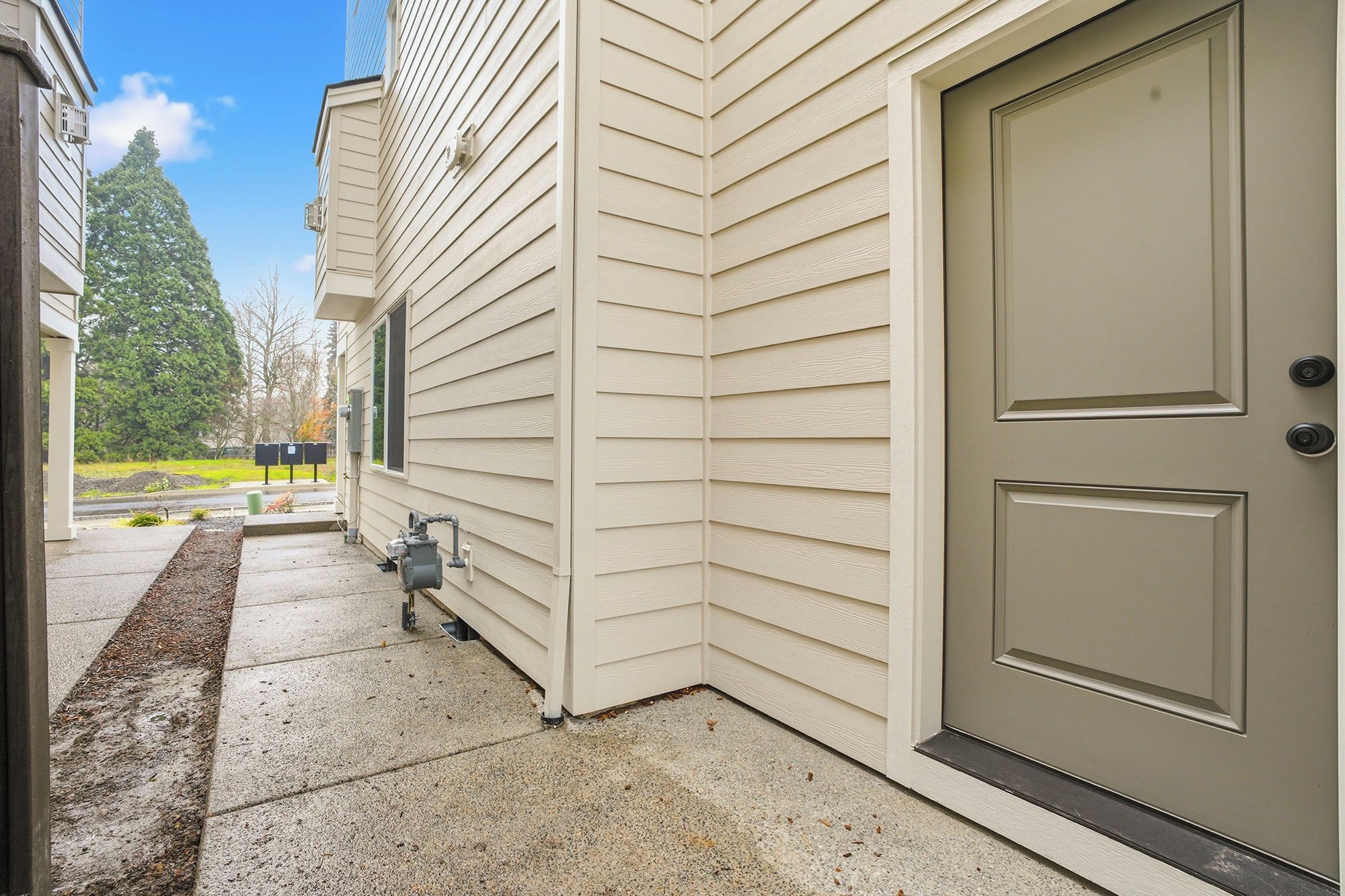 A house exterior with a beige door, a small outdoor utility area, and a clear sky.