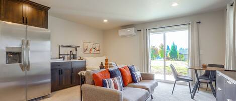A modern kitchen with a refrigerator, a dining area with a table and chairs, and a living room with a sofa.