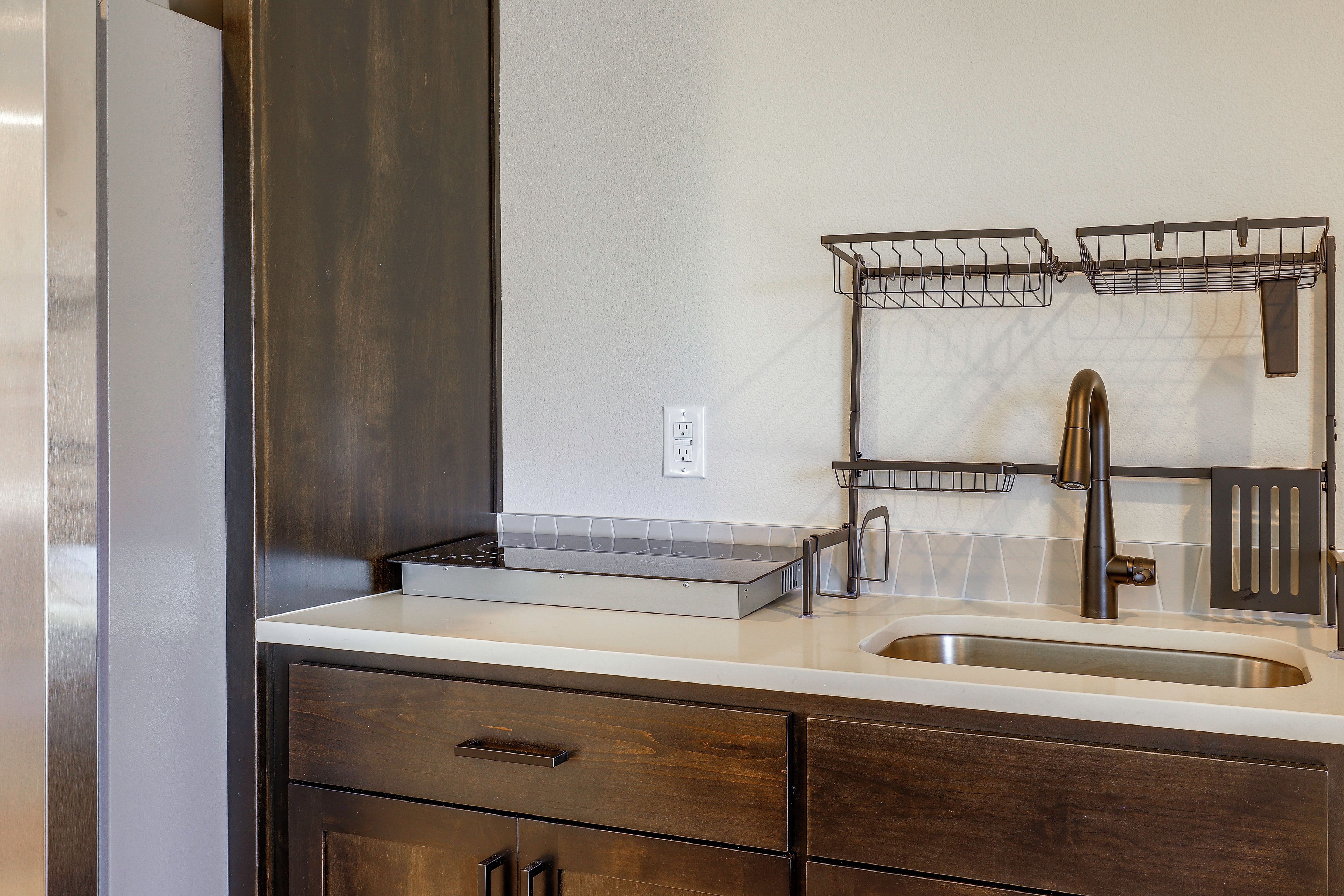 A kitchen with a stainless steel sink, a double hanging rack, and wooden cabinets.