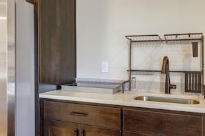 A kitchen with a stainless steel sink, a double hanging rack, and wooden cabinets. - PNW Home Base! Gresham Studio w/ Patio (Gresham)