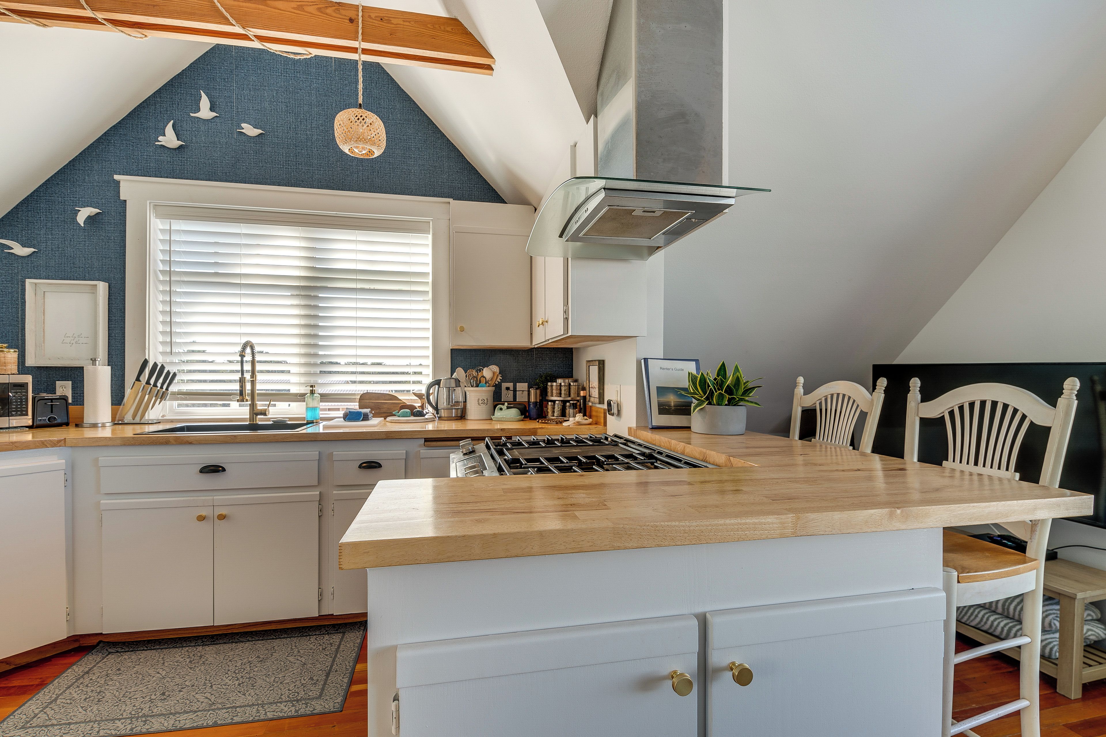 A modern kitchen with a central island, white cabinetry, and a large window with blinds.
