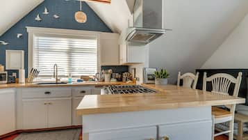 A modern kitchen with a central island, white cabinetry, and a large window with blinds.
