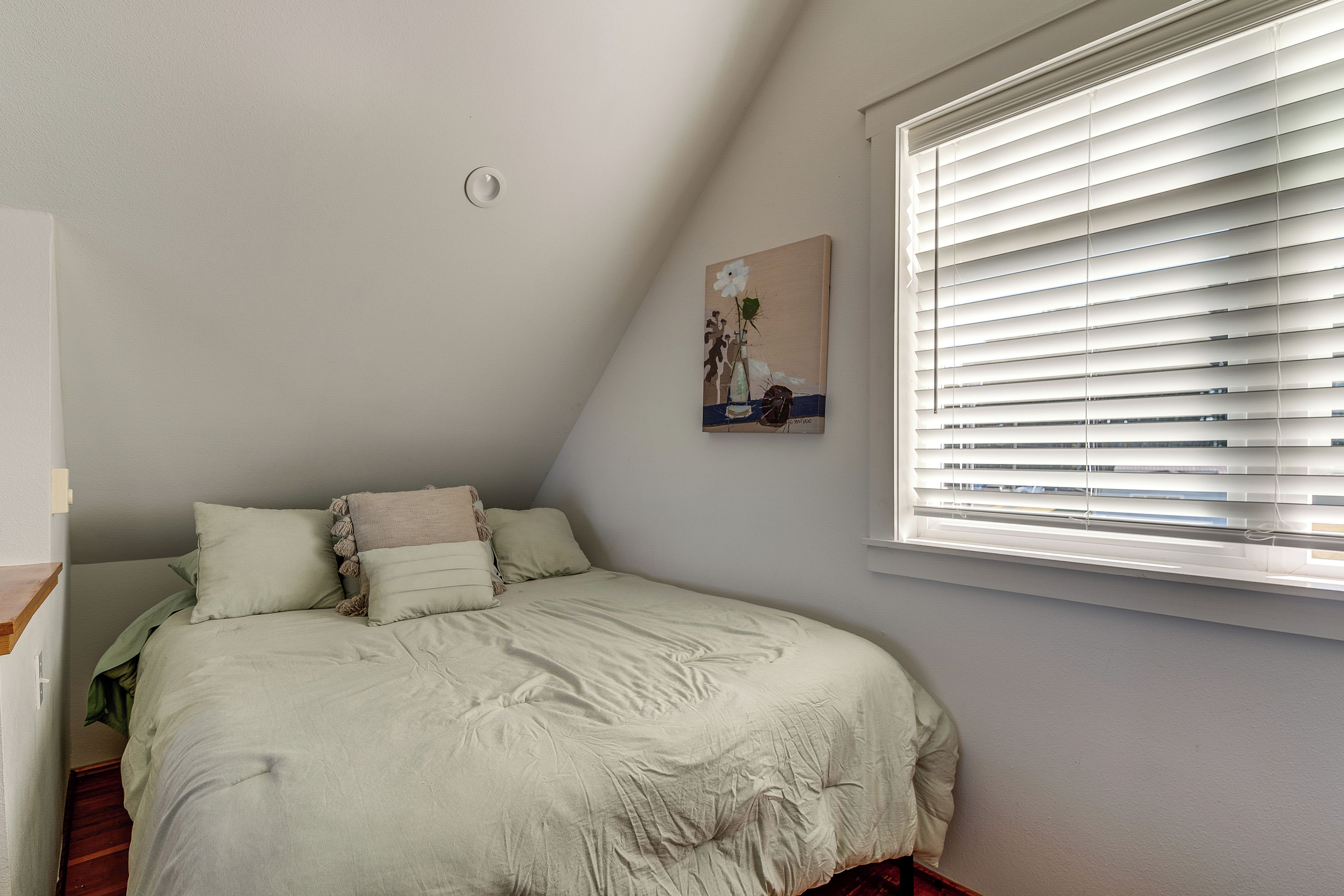 A bedroom with a bed, pillows, a painting, and a window with blinds.