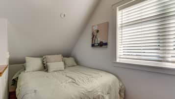 A bedroom with a bed, pillows, a painting, and a window with blinds.