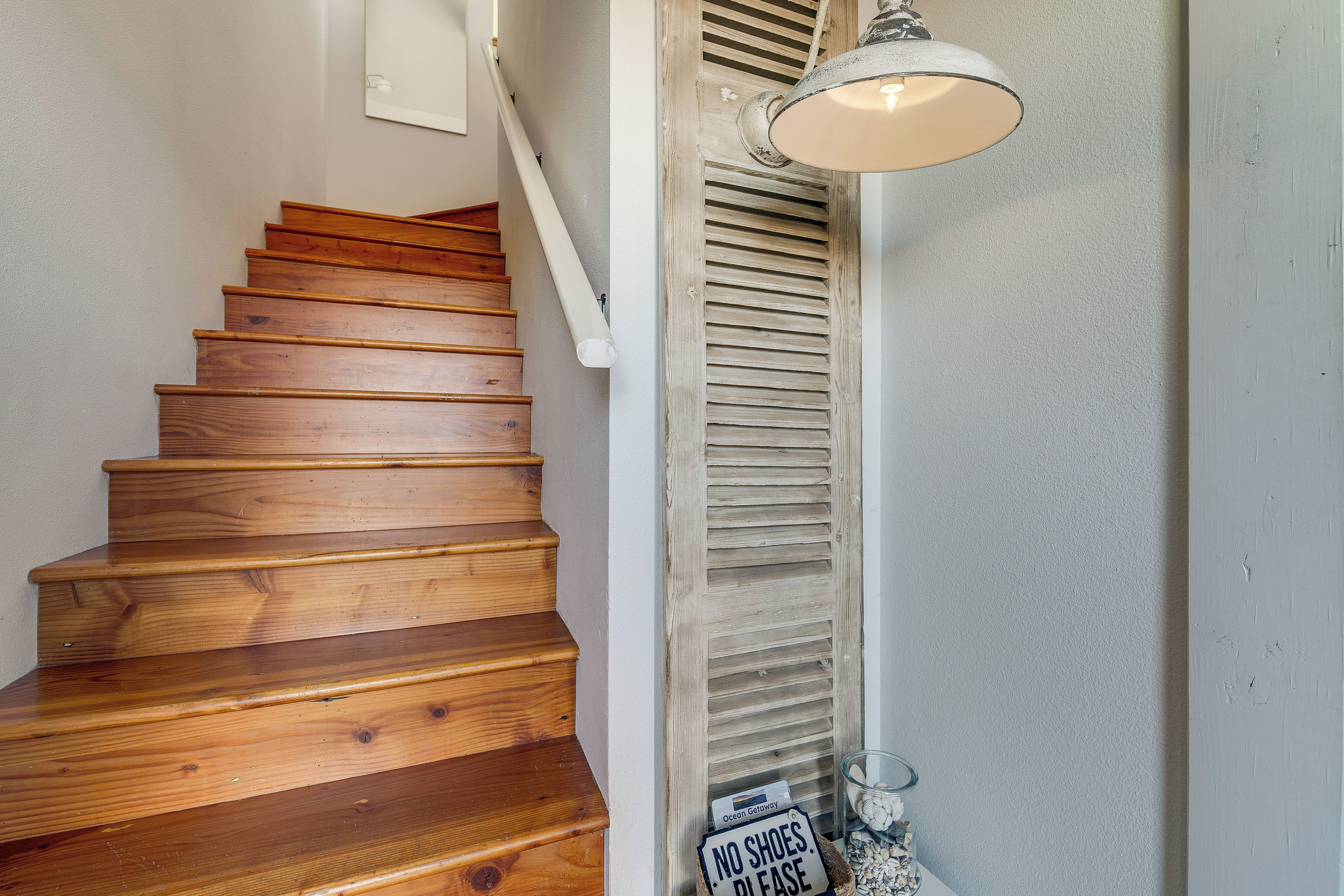 A wooden staircase with a 'NO SHOES PLEASE' sign, a white wall, and a hanging light fixture.