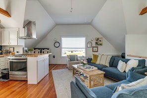 Cozinha moderna com ilha central, área de refeições com sofá e mesa de centro, e uma janela ampla que oferece luz natural.