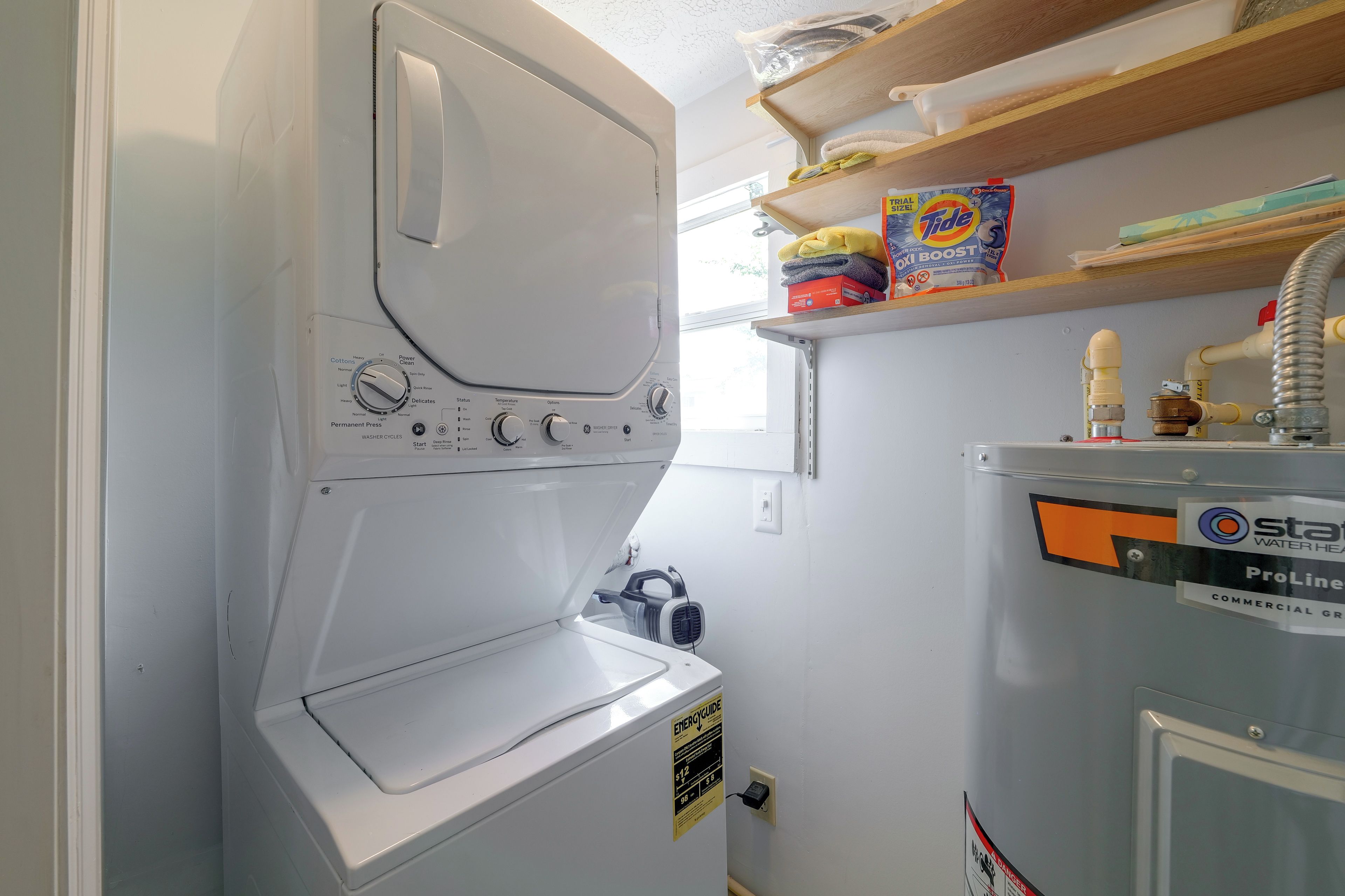 A compact, white front-loading washing machine with multiple settings, a water heater, and a ProLine water heater on the wall.