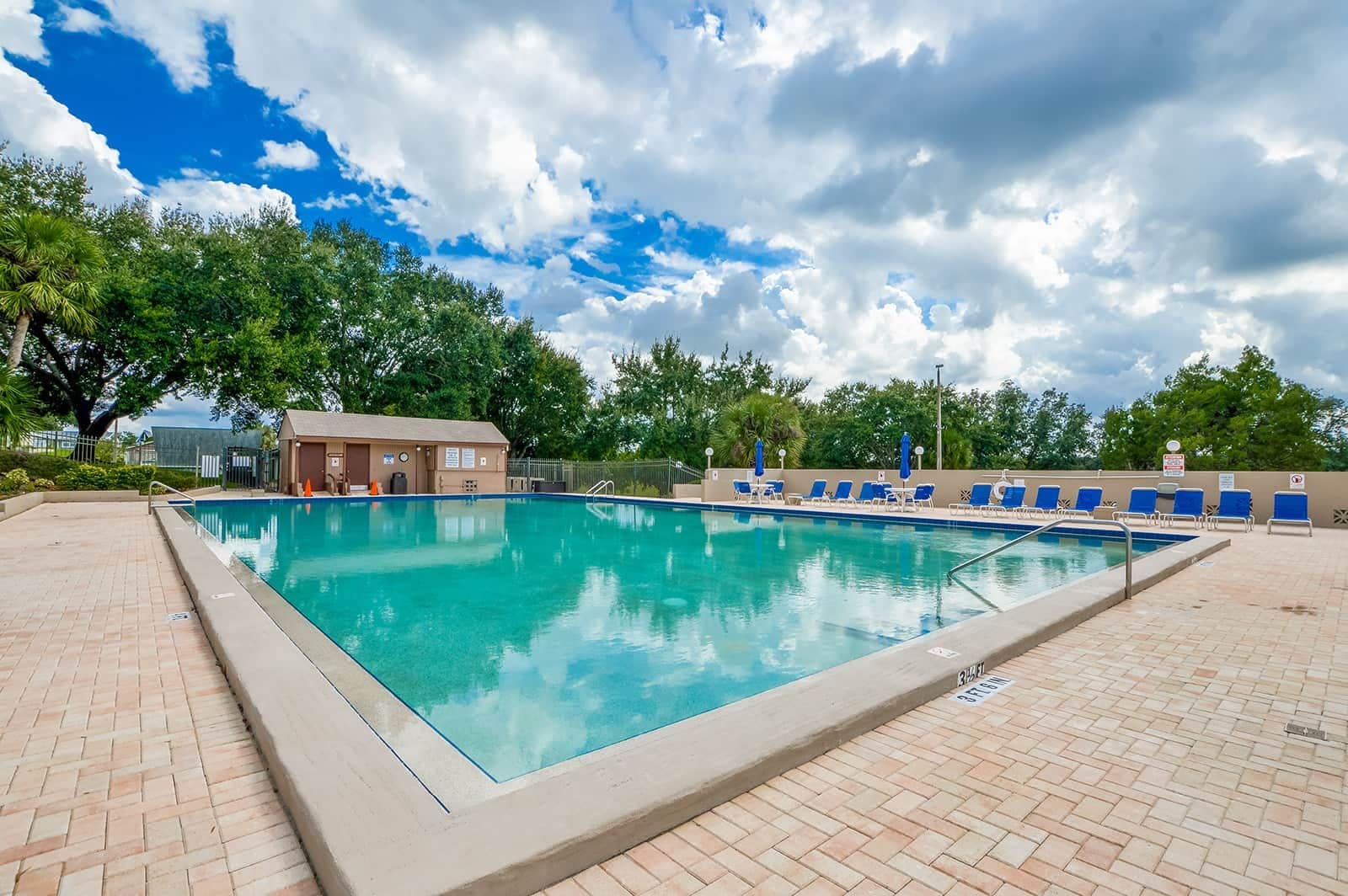 Una piscina con solárium de baldosas, vestuario y sillas de descanso.