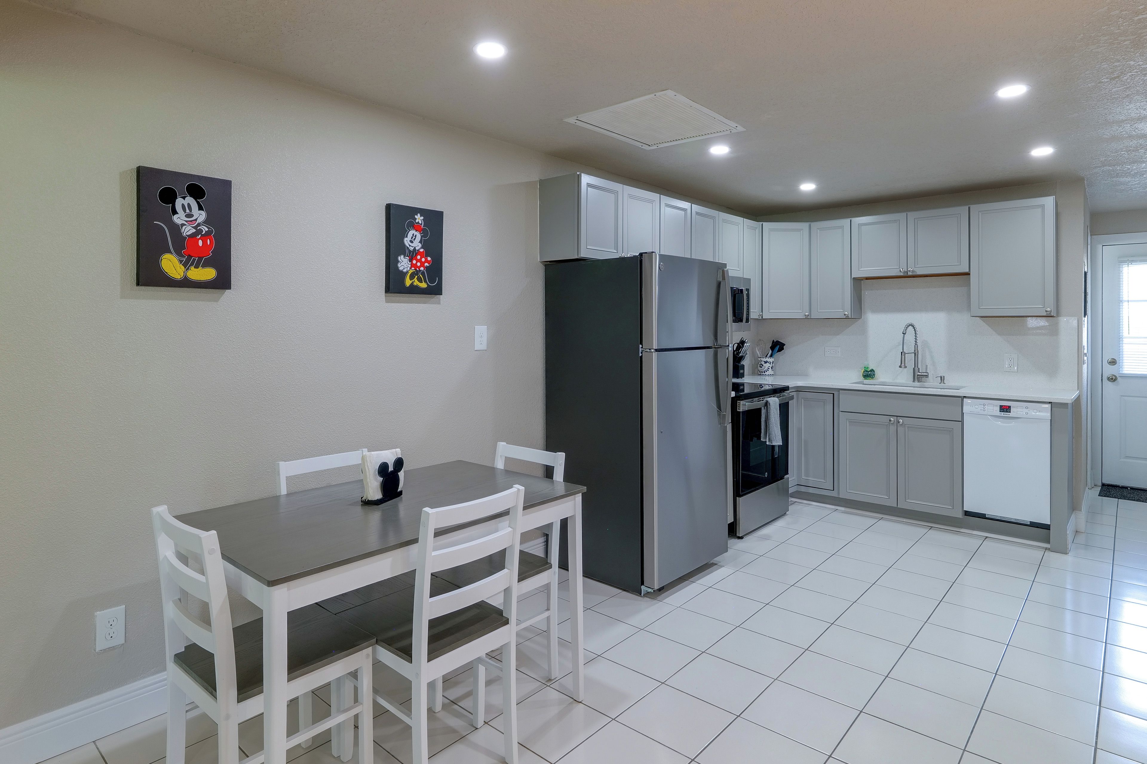A modern kitchen with white cabinets, a stainless steel refrigerator, and a dining area with a table and chairs.