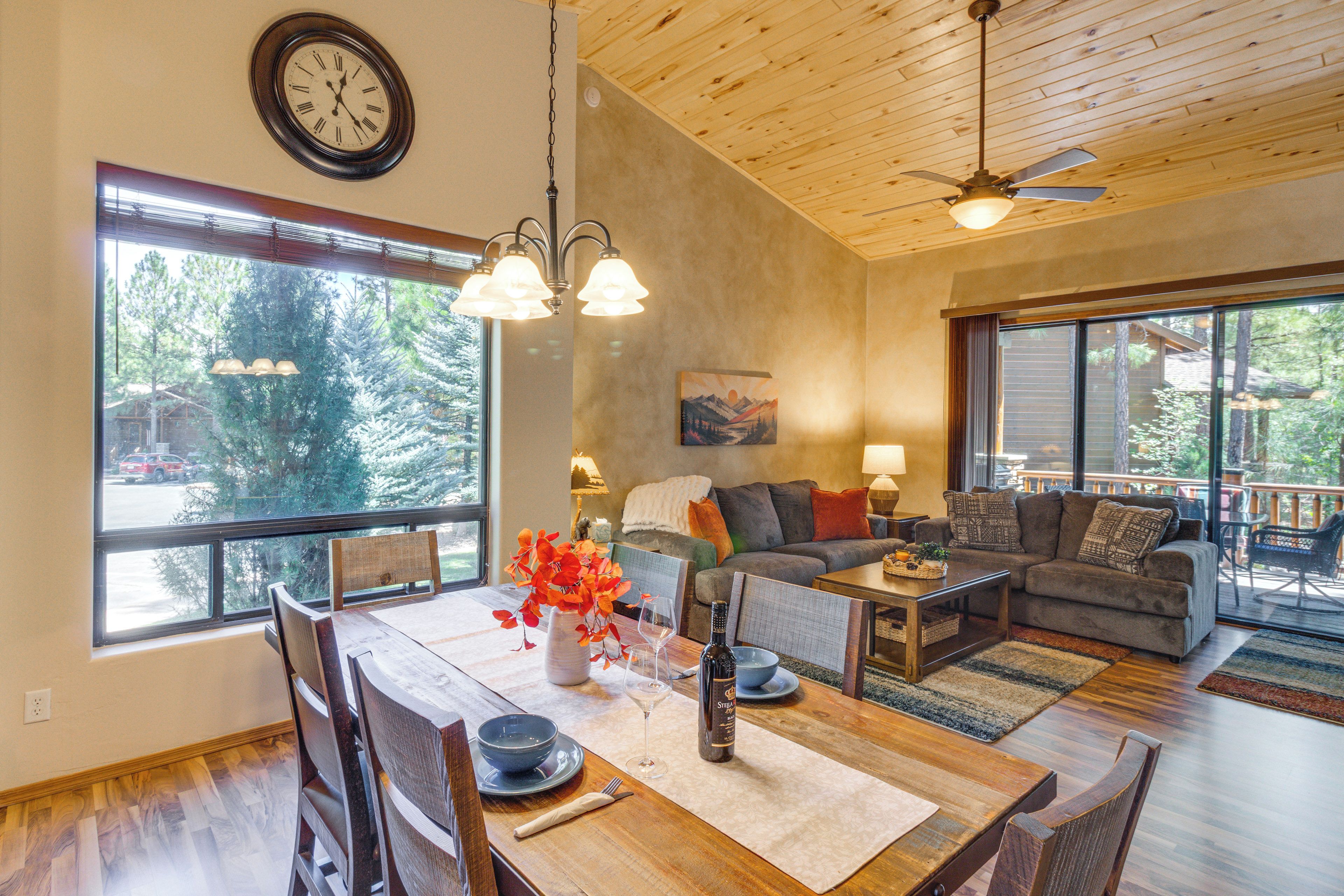 A spacious living area with a dining table, seating, and large windows offering a view of trees.