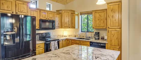 A kitchen with wooden cabinets, a stainless steel refrigerator, a microwave, a stove, and a large marble countertop.