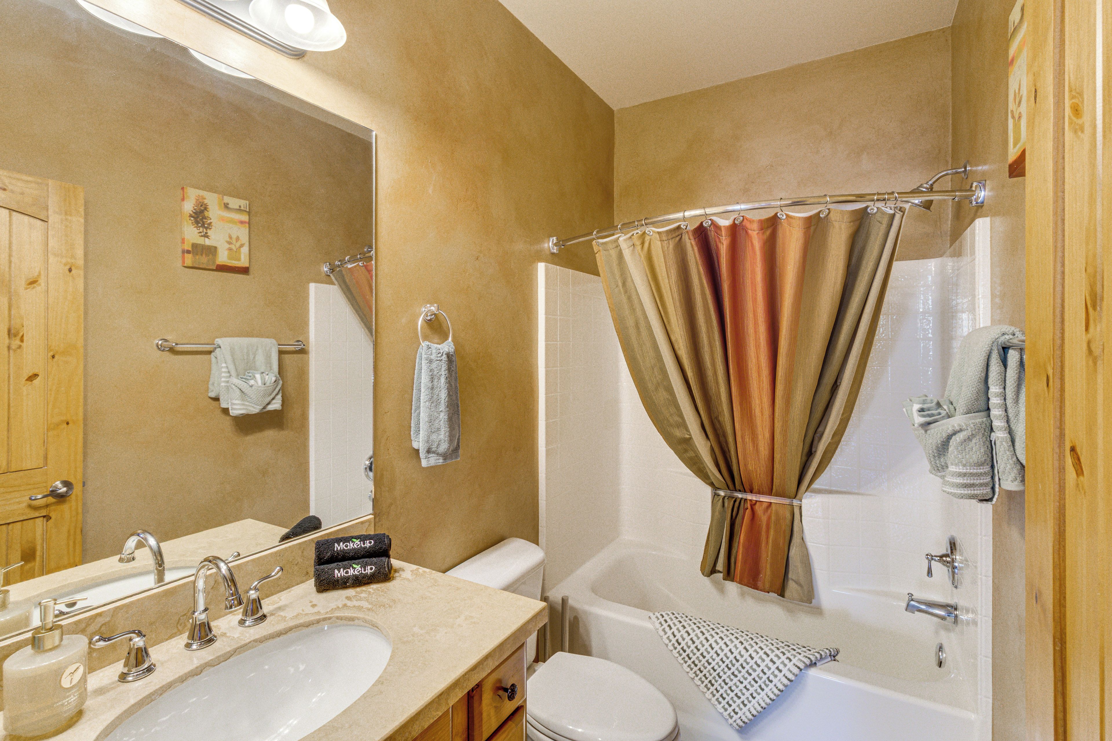 A bathroom with a sink, mirror, toilet, and shower curtain.