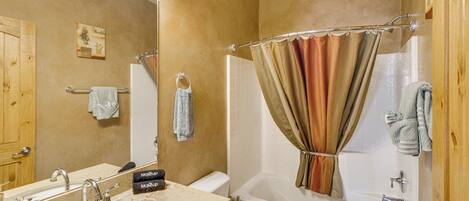 A bathroom with a sink, mirror, toilet, and shower curtain.