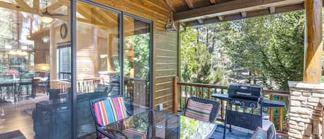 A covered outdoor seating area with glass walls, wicker furniture, and a stone wall.