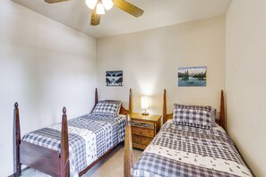 Quarto com duas camas de madeira, uma mesa de cabeceira com abajur e duas pinturas penduradas na parede.