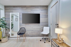 A modern room with a large flat-screen TV mounted on the wall, a black office chair, a white chair, a wooden side table with a lamp, and a potted plant. - Tannersville Mtn Escape: Ski, Hike & Shop! (Tannersville)