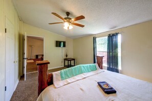 A bedroom with a bed, a ceiling fan, a TV mounted on the wall, and a window with curtains.