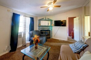 Una sala de estar con ventilador de techo, chimenea, televisor y sofá.
