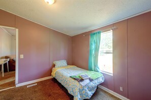 A bedroom with a single bed, a window with curtains, a desk, and a chair.