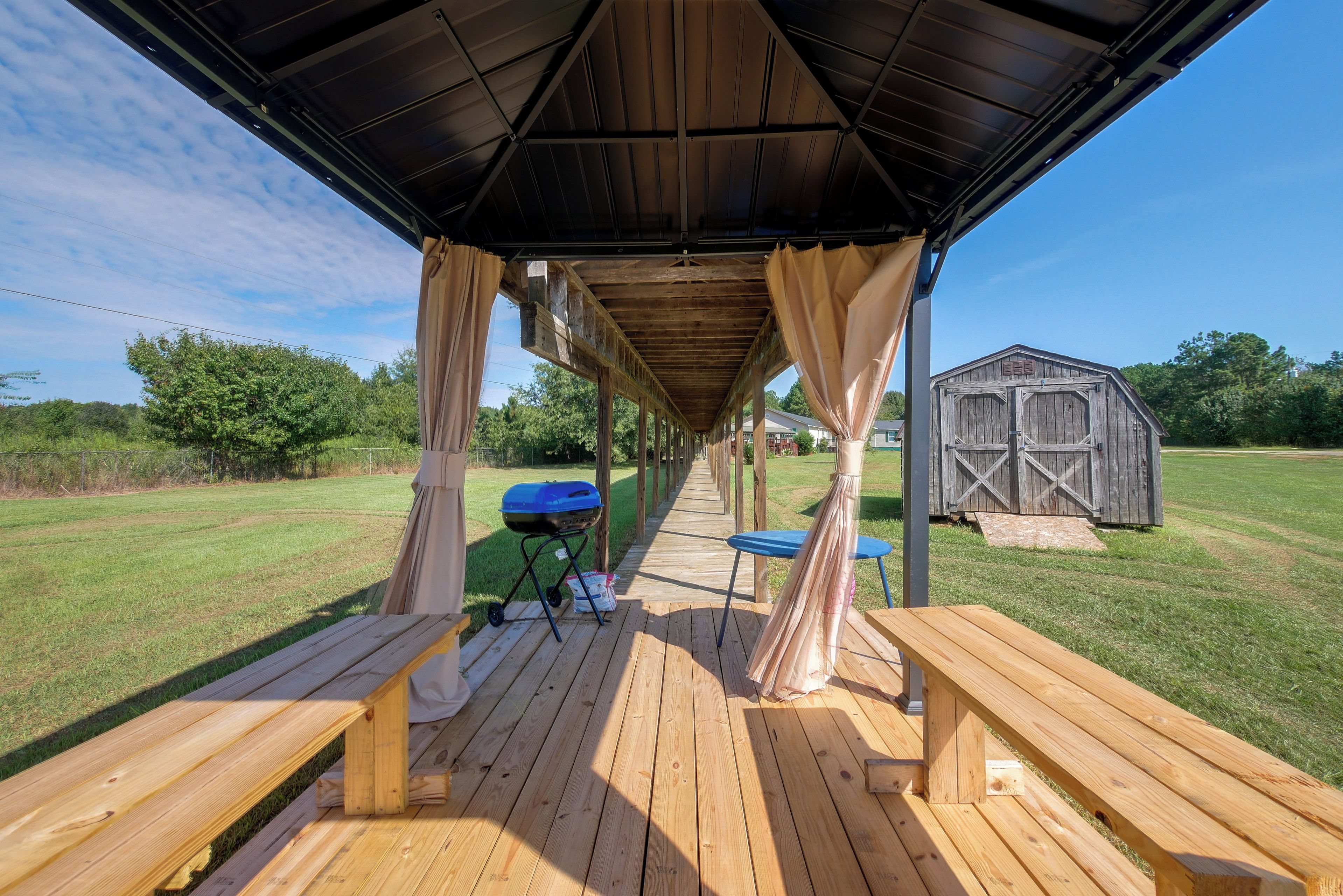 An outdoor covered patio with wooden benches and a grill.