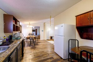 A kitchen with wooden cabinets, a refrigerator, a dining table with chairs, and a kitchen island with a sink and utensils.