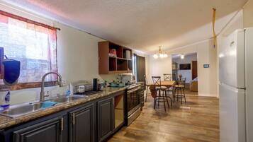 A kitchen with a central island, dark cabinetry, a stainless steel sink, and a dining area with a table and chairs.