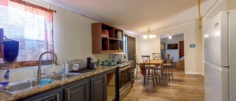 A kitchen with a central island, dark cabinetry, a stainless steel sink, and a dining area with a table and chairs.