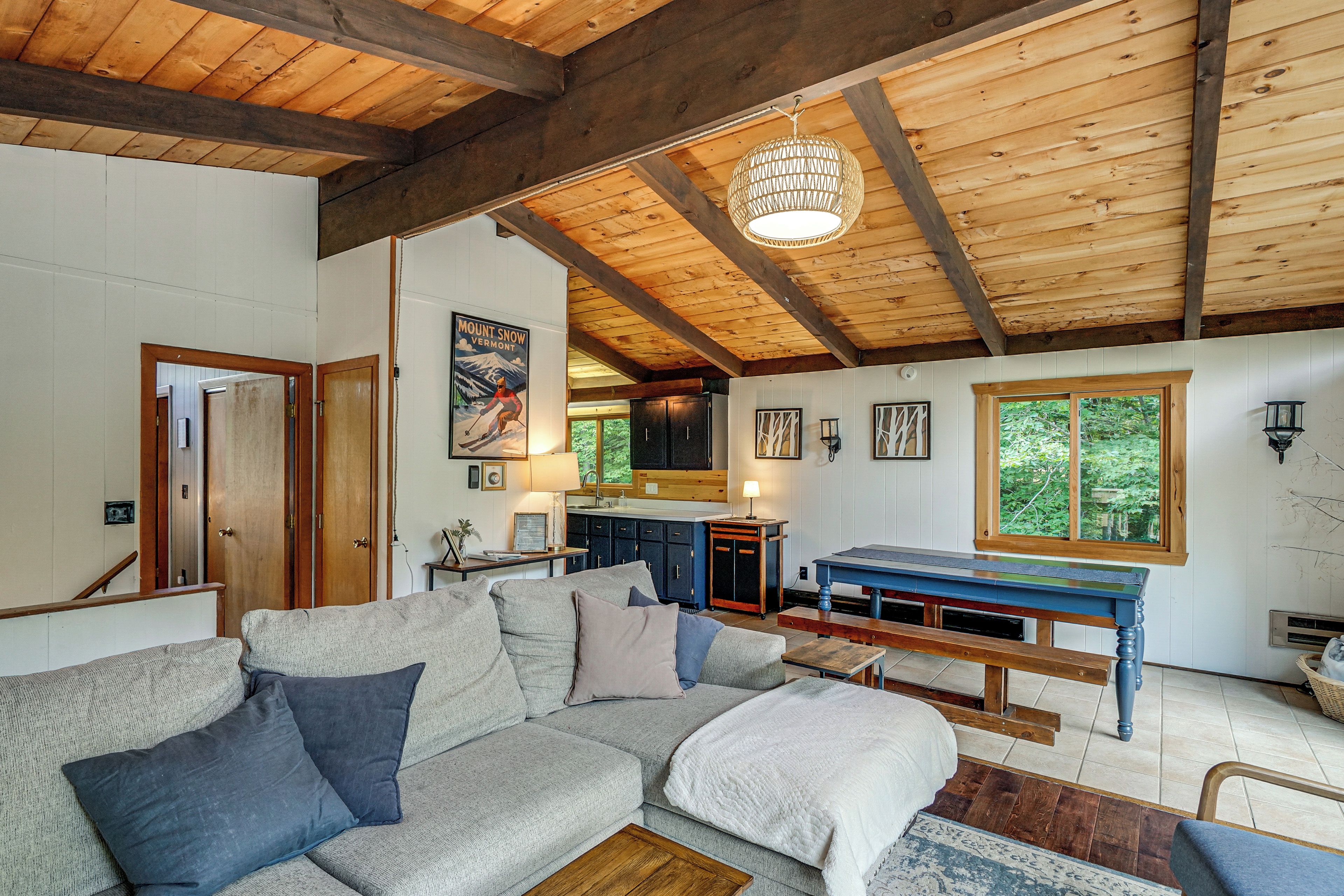 A cozy living room with a wooden ceiling, a sofa, a table, and a view of the outdoors.