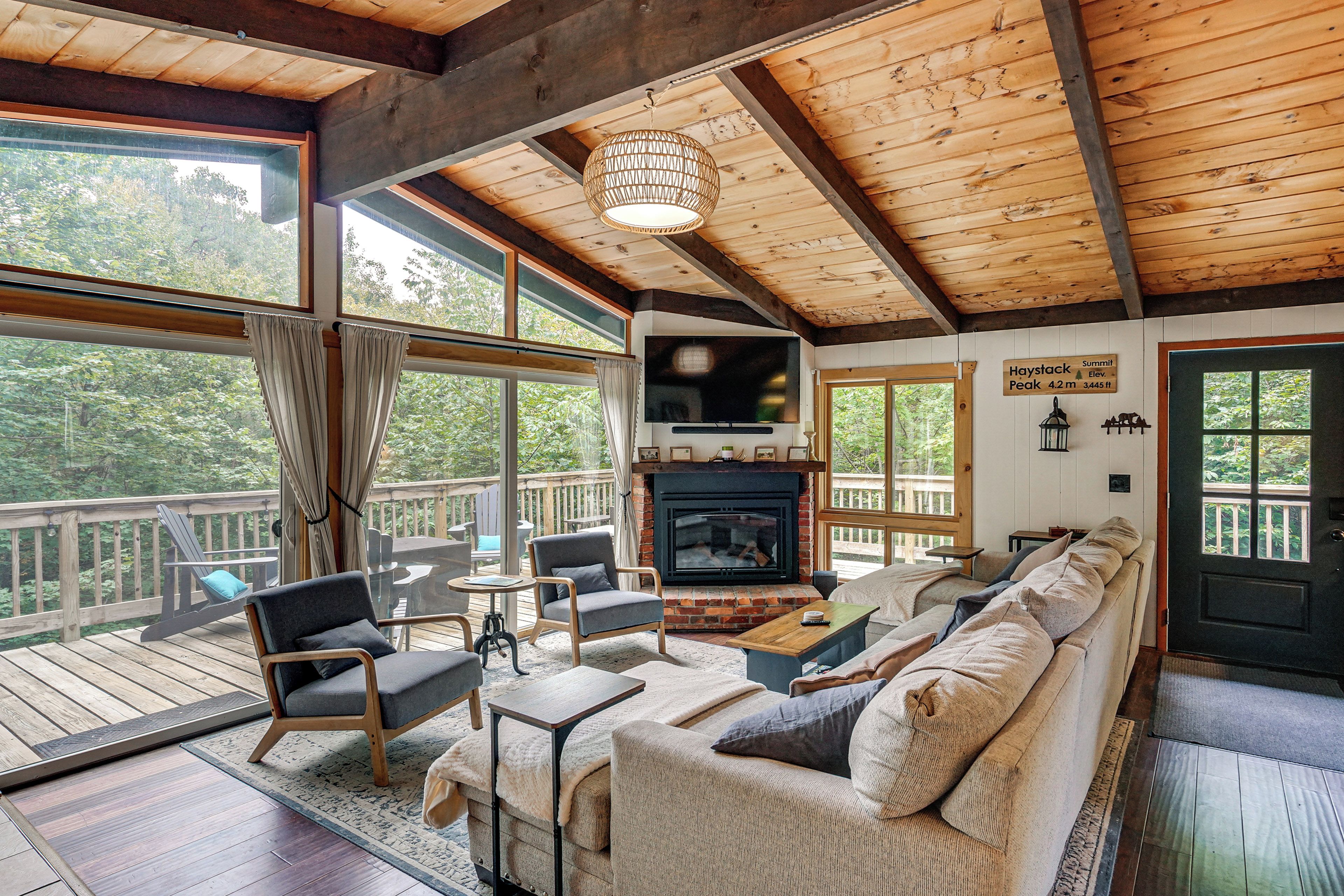 A cozy living room with a fireplace, comfortable seating, and large windows offering a view of the outdoors.