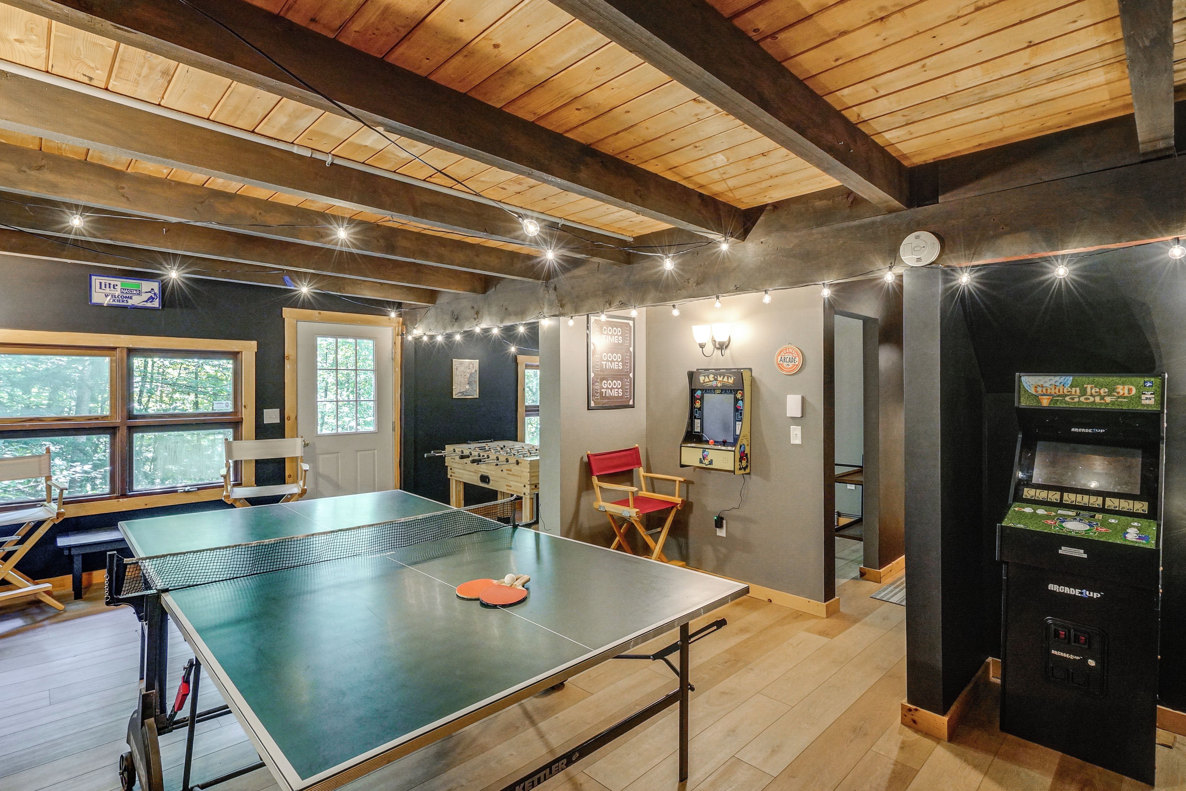 A room with a ping pong table, a foosball table, and a video game machine.