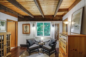 A room with wooden beams, a fireplace, a window with a forest view, two armchairs, a wooden cabinet, and a welcome sign. - Great for Groups! Wilmington Gem w/ Game Room (Wilmington)