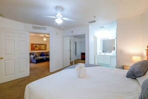 A hotel room with a bed, a ceiling fan, a door leading to a bathroom, and a hallway with a mirror and a door. - Pool Access! Kissimmee Gem, Enclosed Patio (Kissimmee)