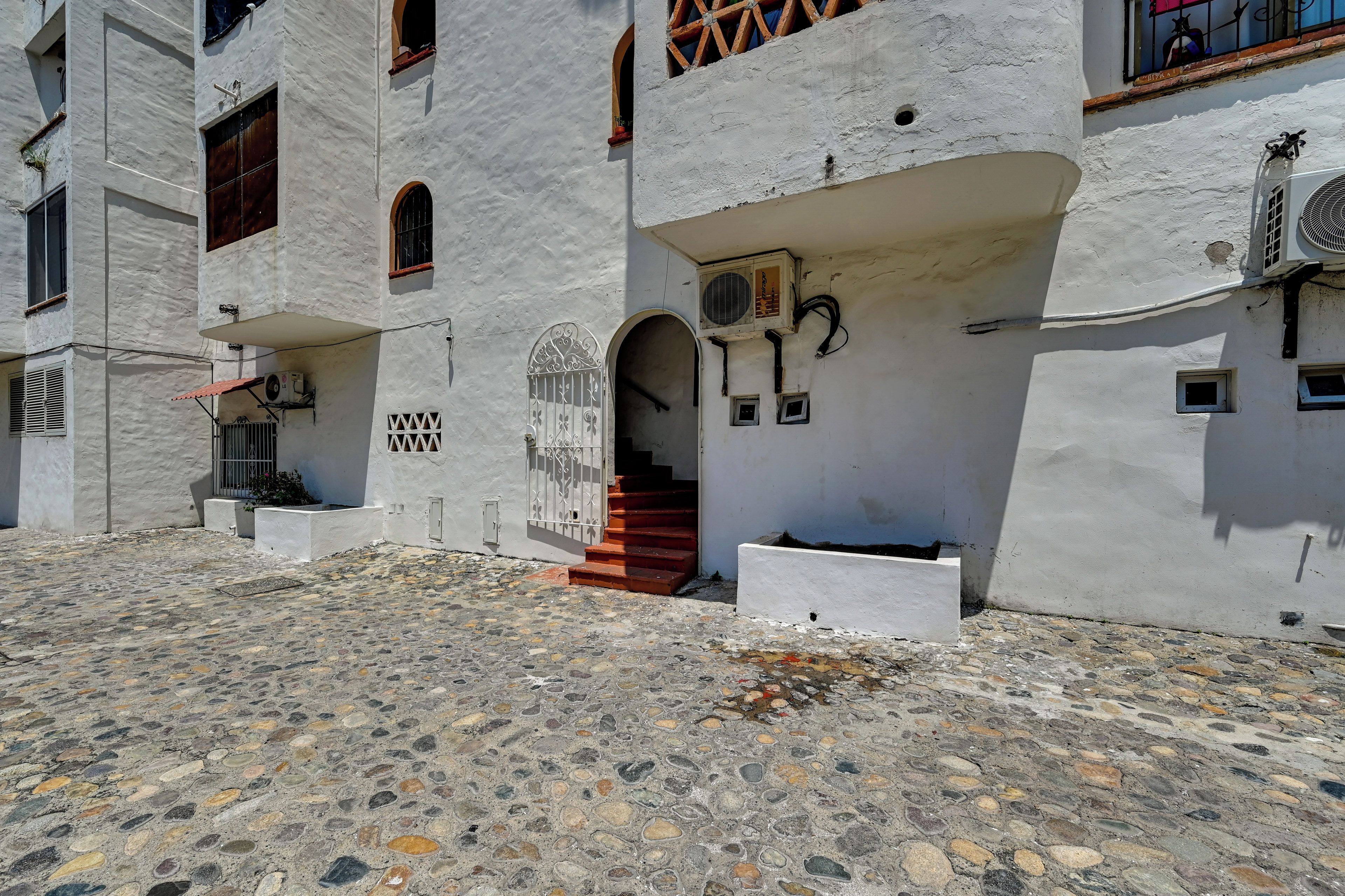 A building with a stone-paved entrance, a staircase leading to an upper level, and a door with decorative metalwork.