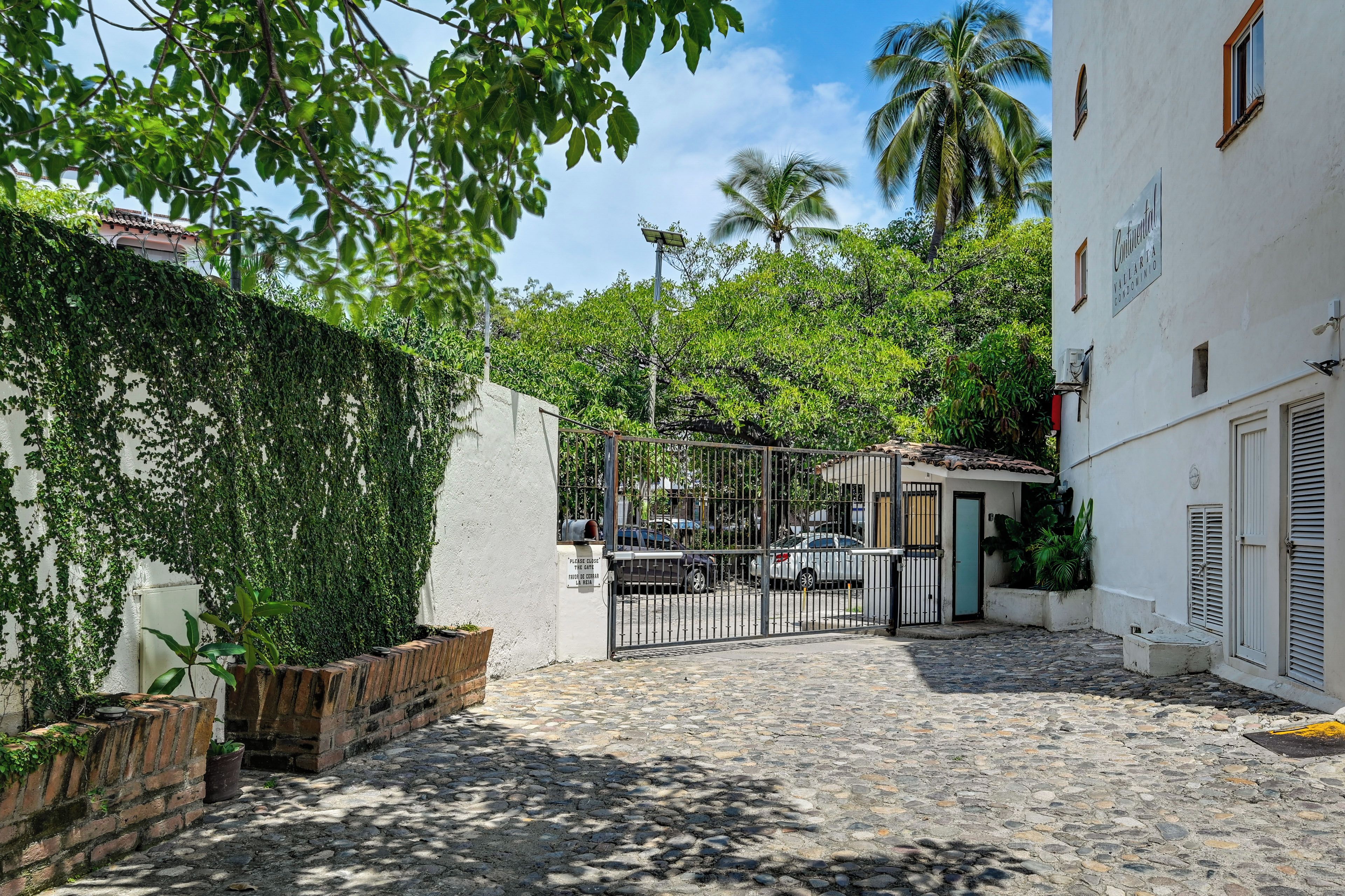 Ruas de paralelepípedos levam a um portão com um edifício branco à direita.
