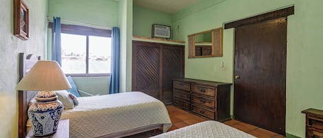 Une chambre avec deux lits, un ventilateur de plafond, une fenêtre avec des rideaux, une commode et un miroir.