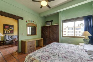 Une pièce comprenant un lit, une commode, un miroir, une fenêtre avec des rideaux et un ventilateur de plafond.